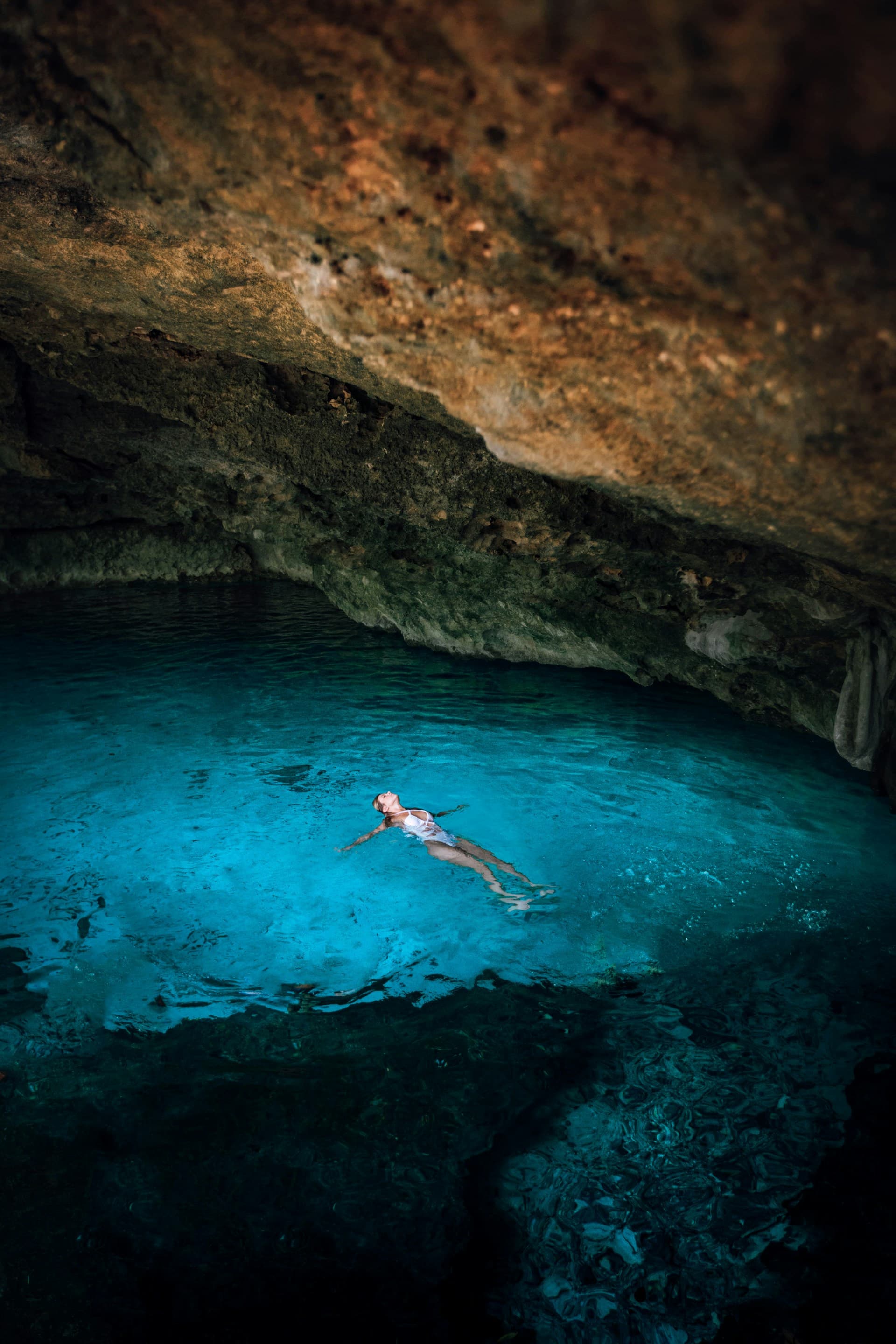 A swimmer floating in the turquoise water of Dos Ojos cenote under a limestone cave opening