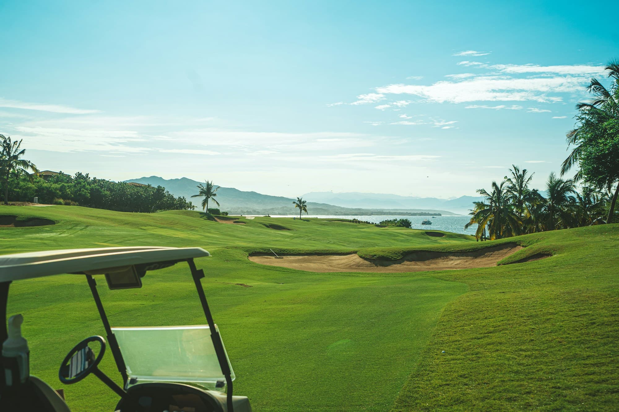 A golf cart on a tropical coastal course with an ocean view