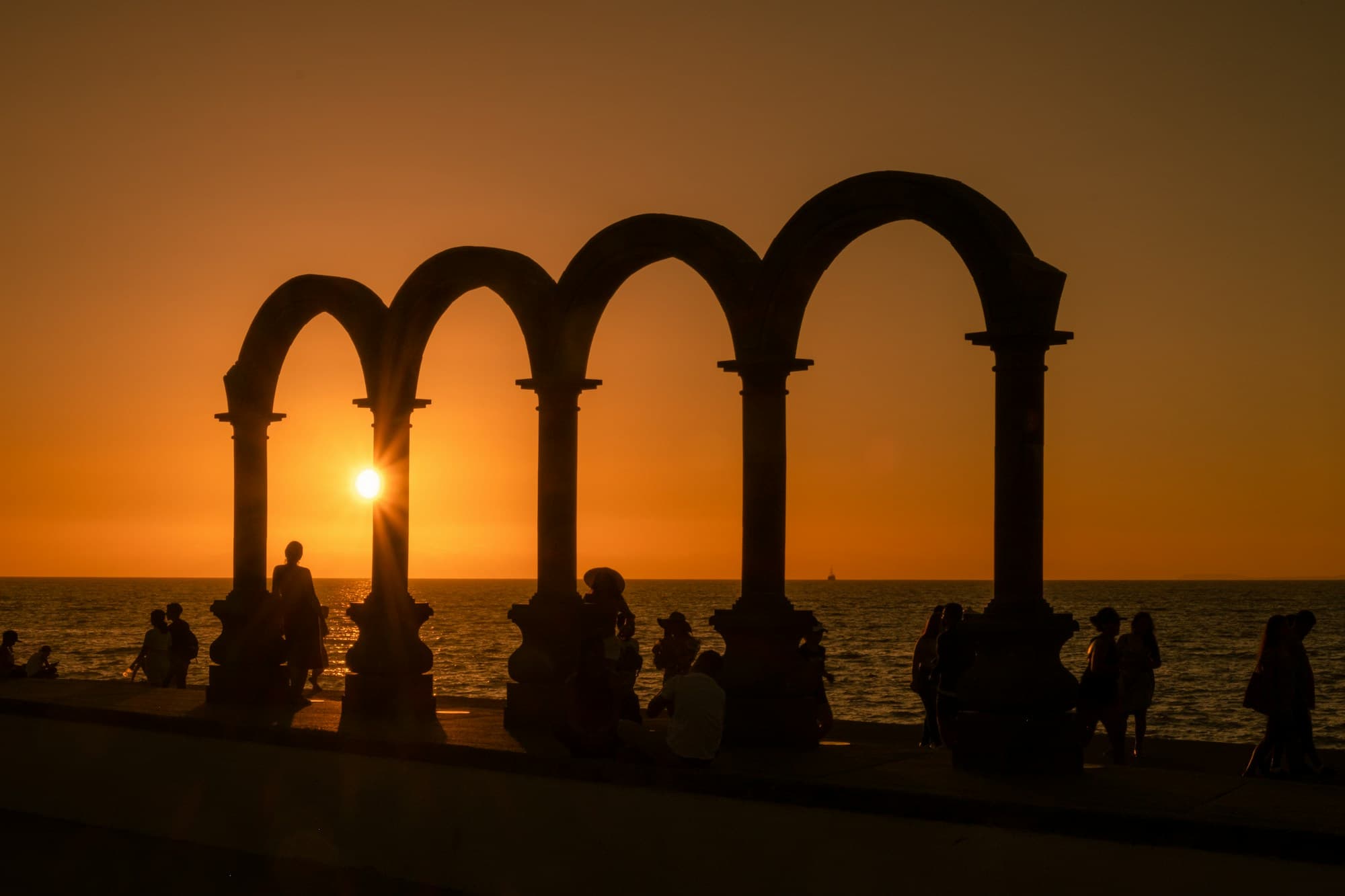 Silhouettes of people walking the Malecón boardwalk at sunset